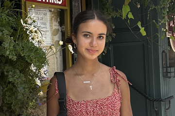 A young person who is smiling and surrounded by greenery.